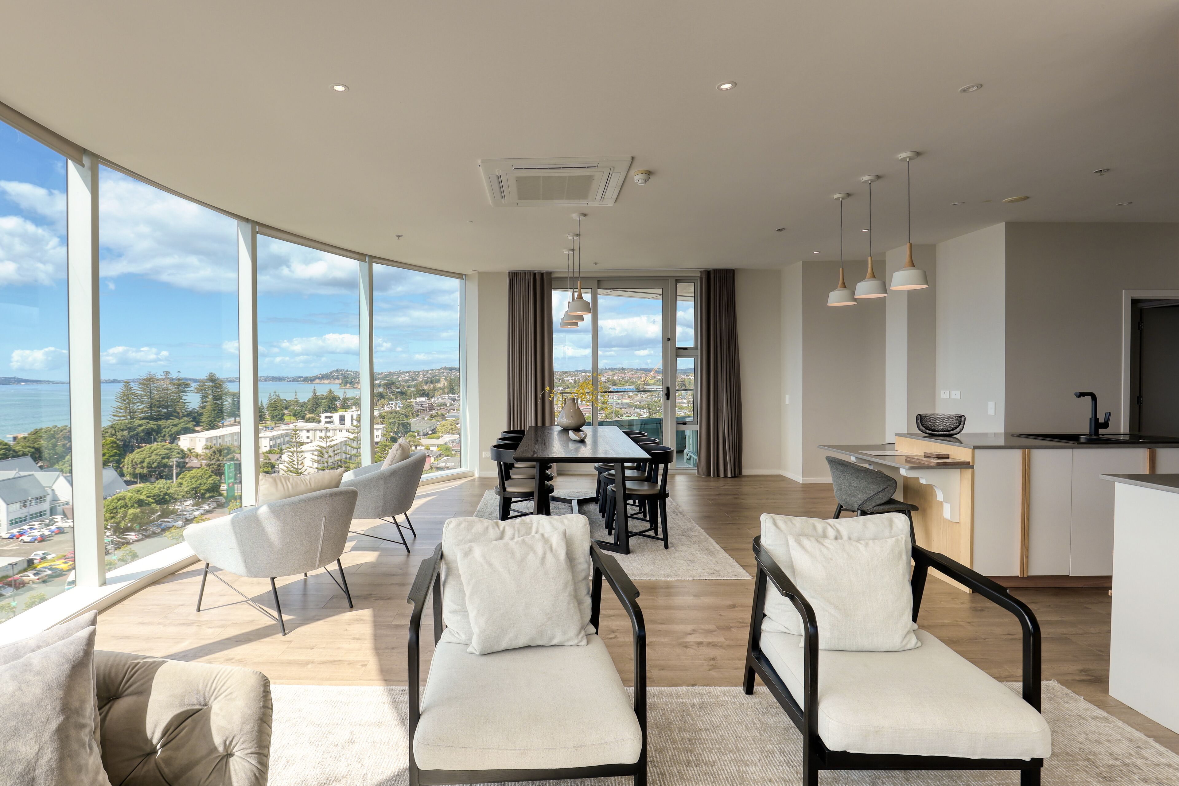 Una sala de estar moderna con una gran mesa de comedor, dos sofás y una zona de cocina con vistas a la ciudad.