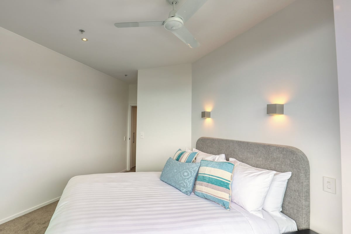 A bedroom with a bed, a ceiling fan, and two wall-mounted light fixtures.