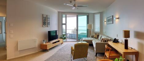 Una sala moderna con televisor de pantalla plana, un sofá, una mesa de centro y una zona de comedor con mesa y sillas de madera.