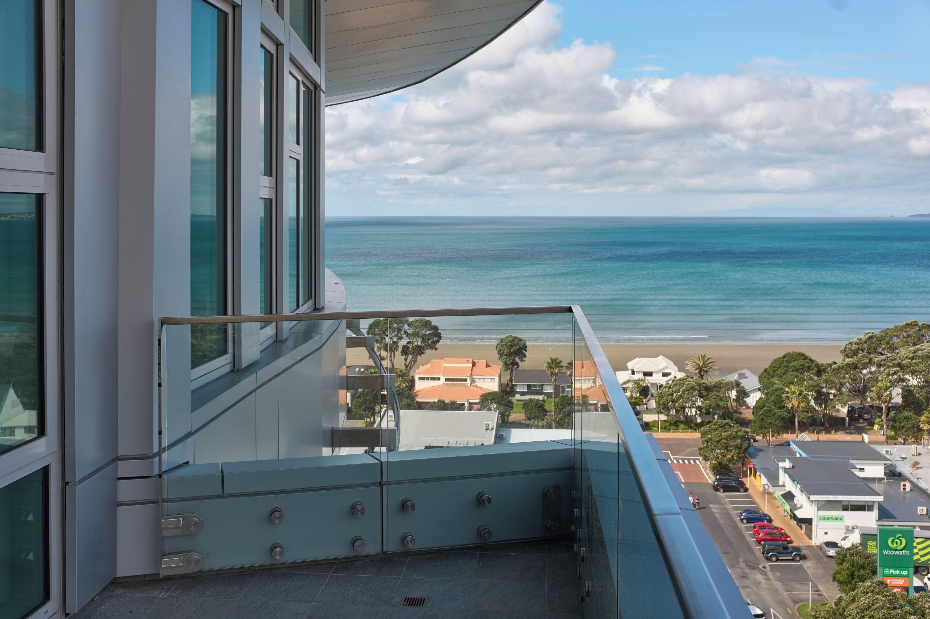 A balcony with a view of the ocean and beach, a building with large windows, and a clear sky.