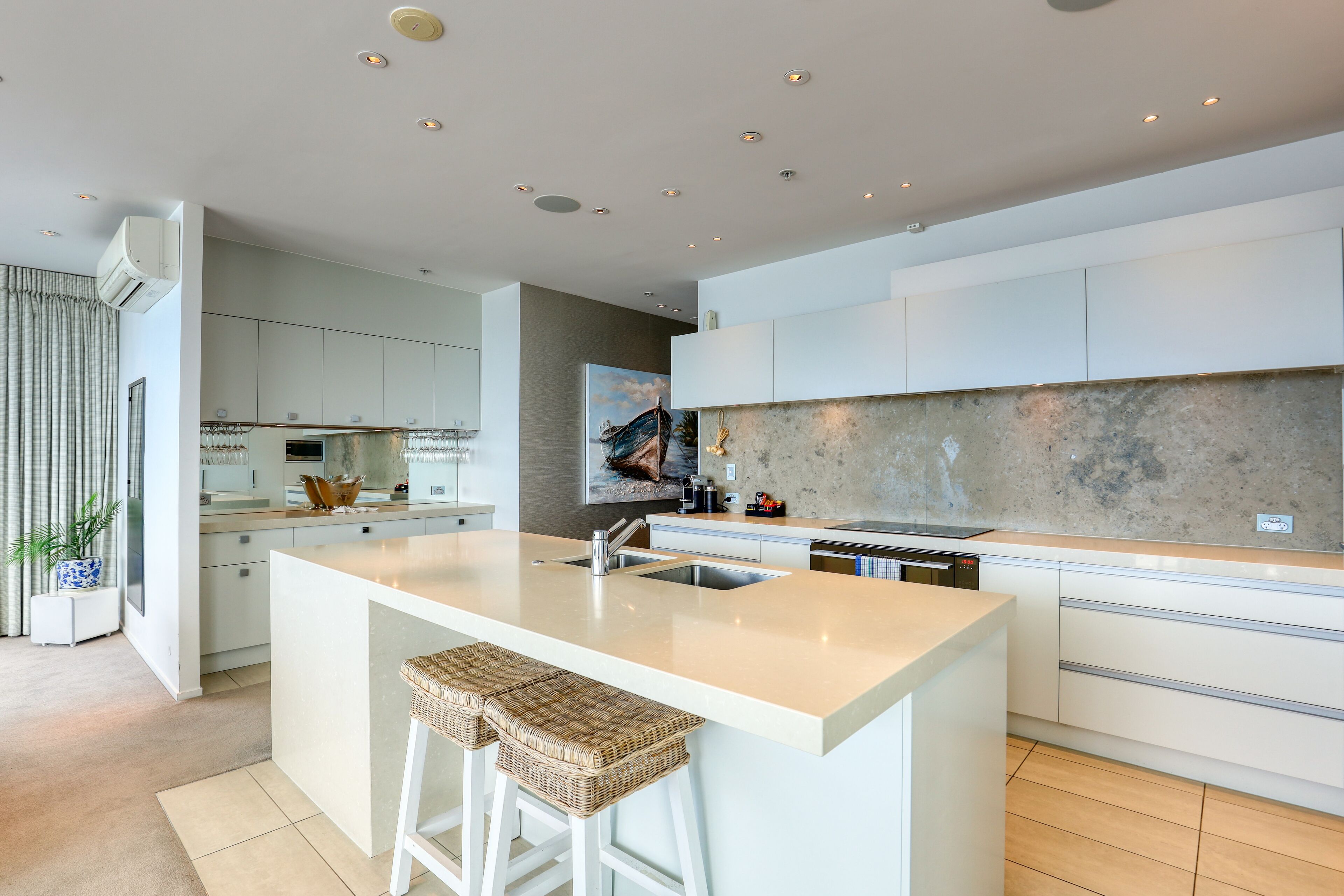 A modern kitchen with a large island, white cabinetry, and a stone backsplash.