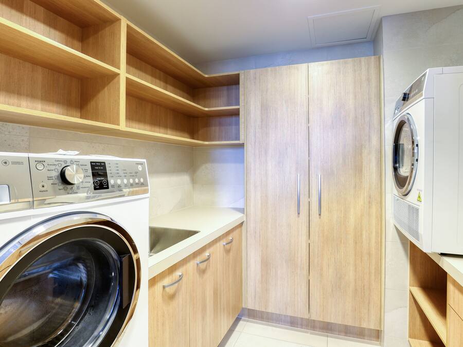 A laundry room with a front-loading washing machine, wooden cabinets, and a countertop.