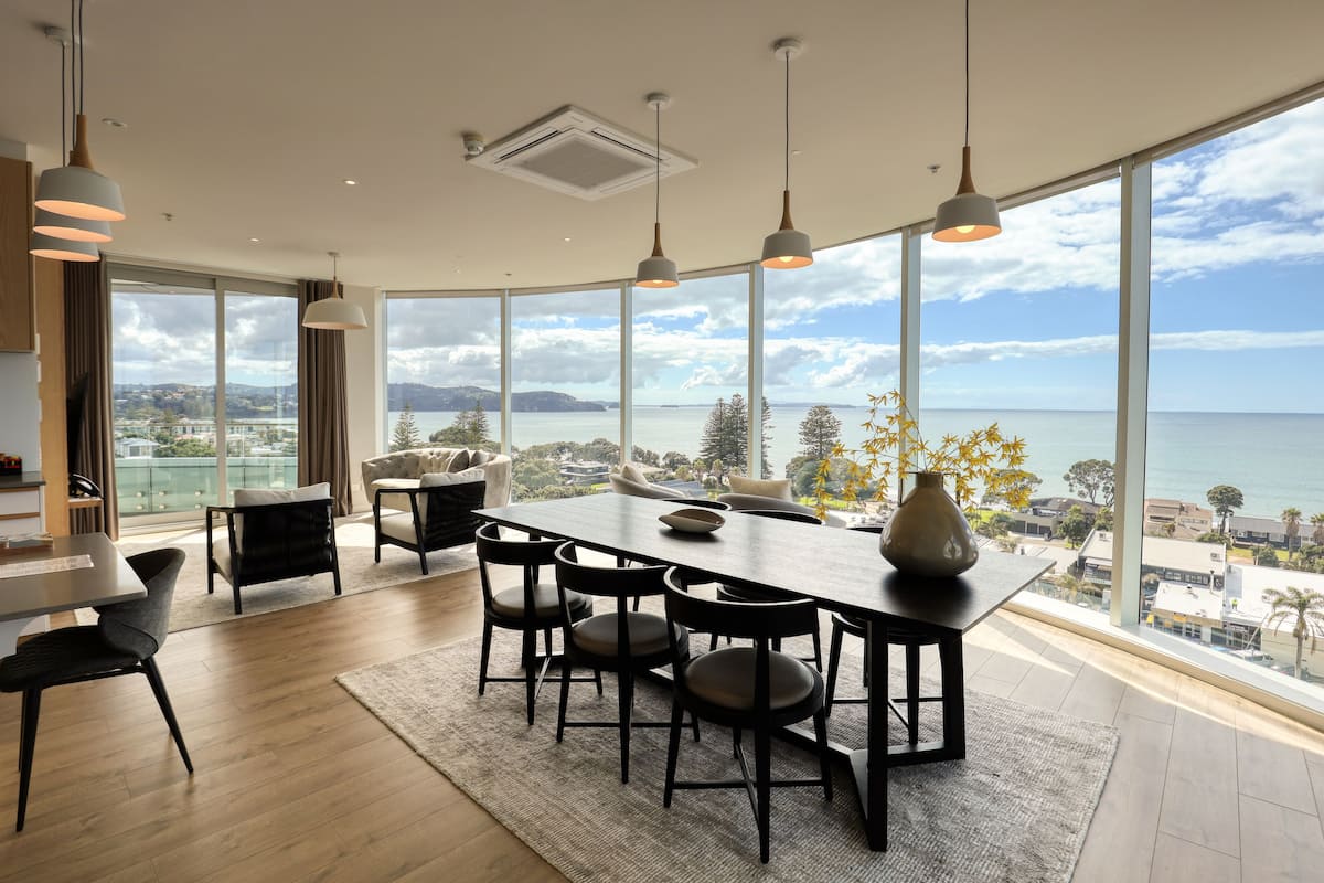 A modern dining area with a large table, chairs, and pendant lights.
