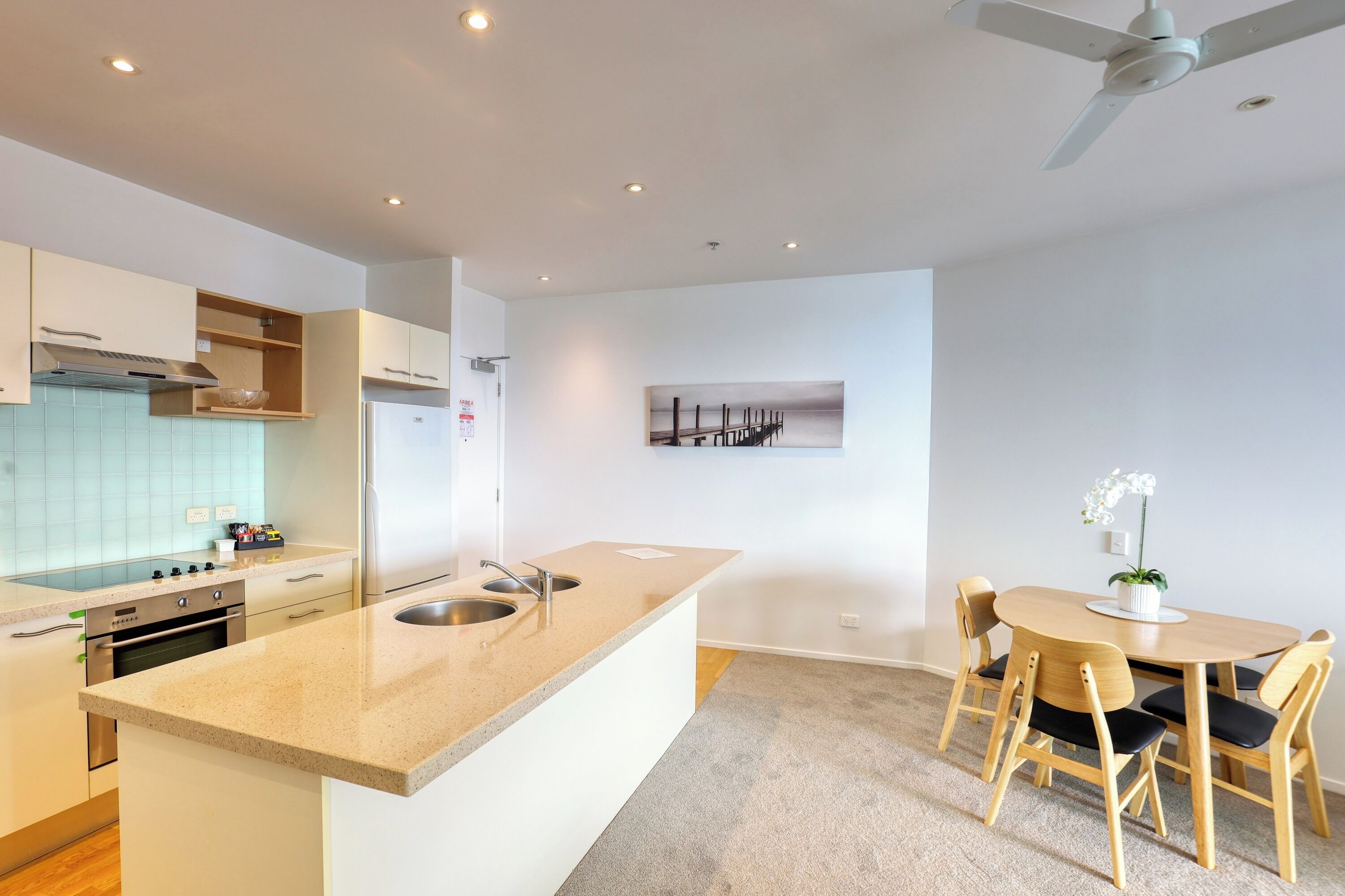 Una cucina moderna con isola centrale, forno integrato e lavello in acciaio inossidabile. È presente una zona pranzo con tavolo e sedie in legno.