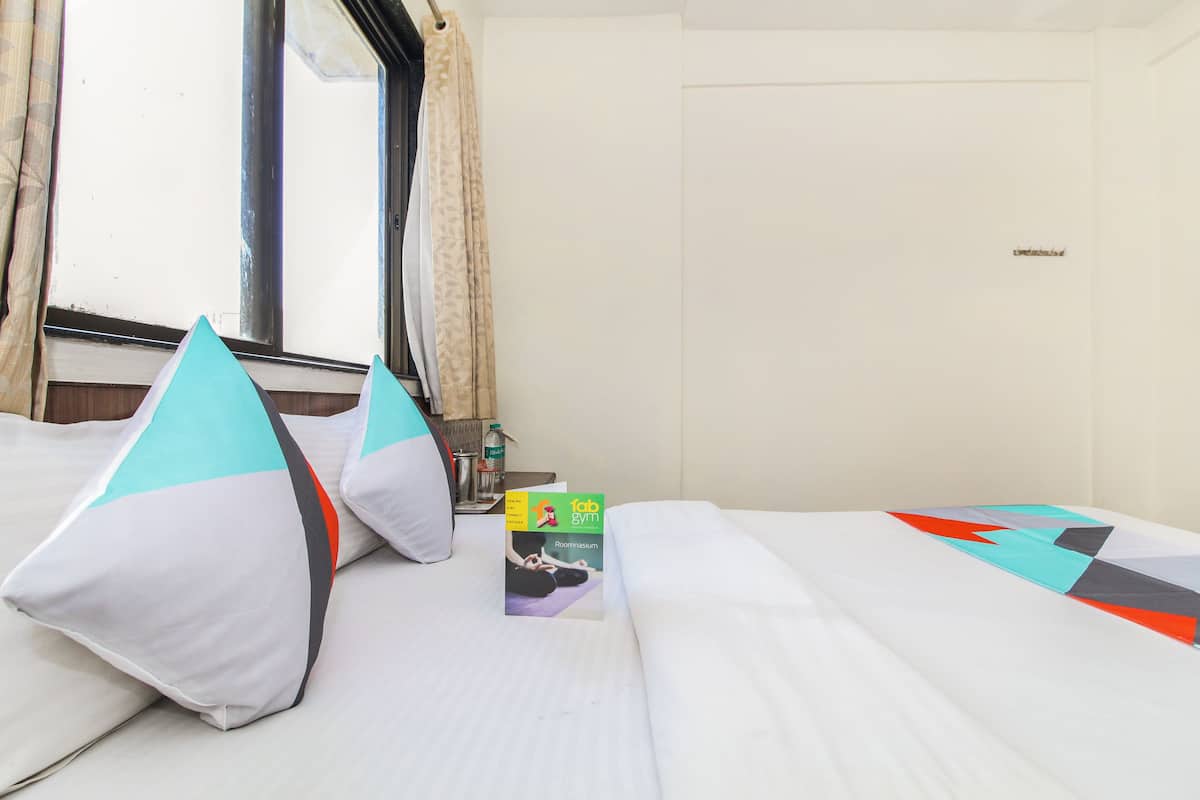A hotel room with a bed, pillows, a book, and a window with curtains.
