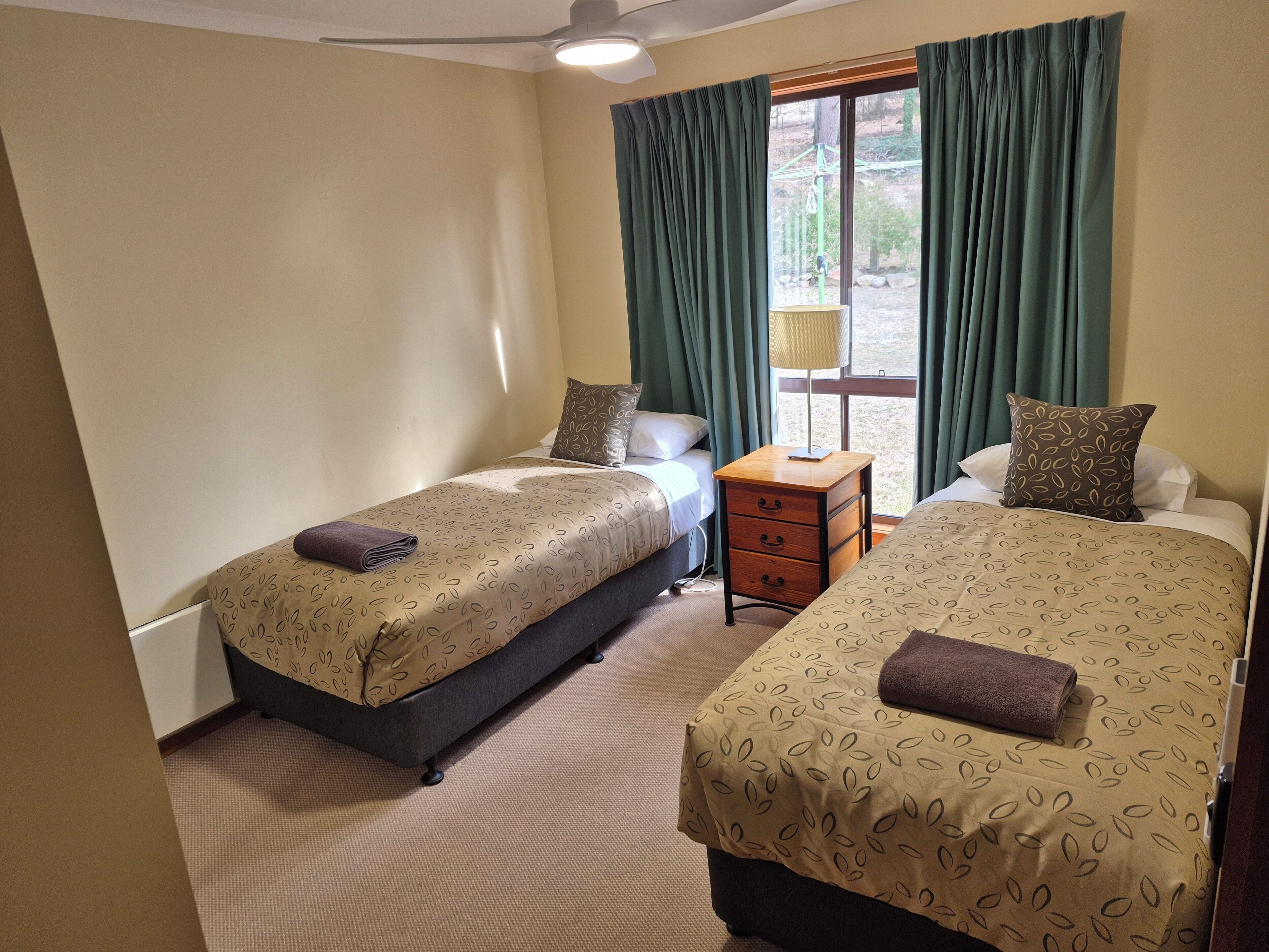 A hotel room with two beds, a bedside table, a lamp, and a window with curtains.