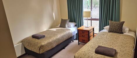 A hotel room with two beds, a bedside table, a lamp, and a window with curtains.