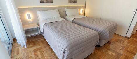 Una habitación de hotel con dos camas, suelo de parqué y lámparas fijadas en la pared.
