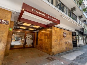 L’extérieur d’un hôtel se distingue par son entrée imposante, une enseigne indiquant « TRIANON - RECOLETA » et une adresse clairement visible : « 1869, avenue Callao ».