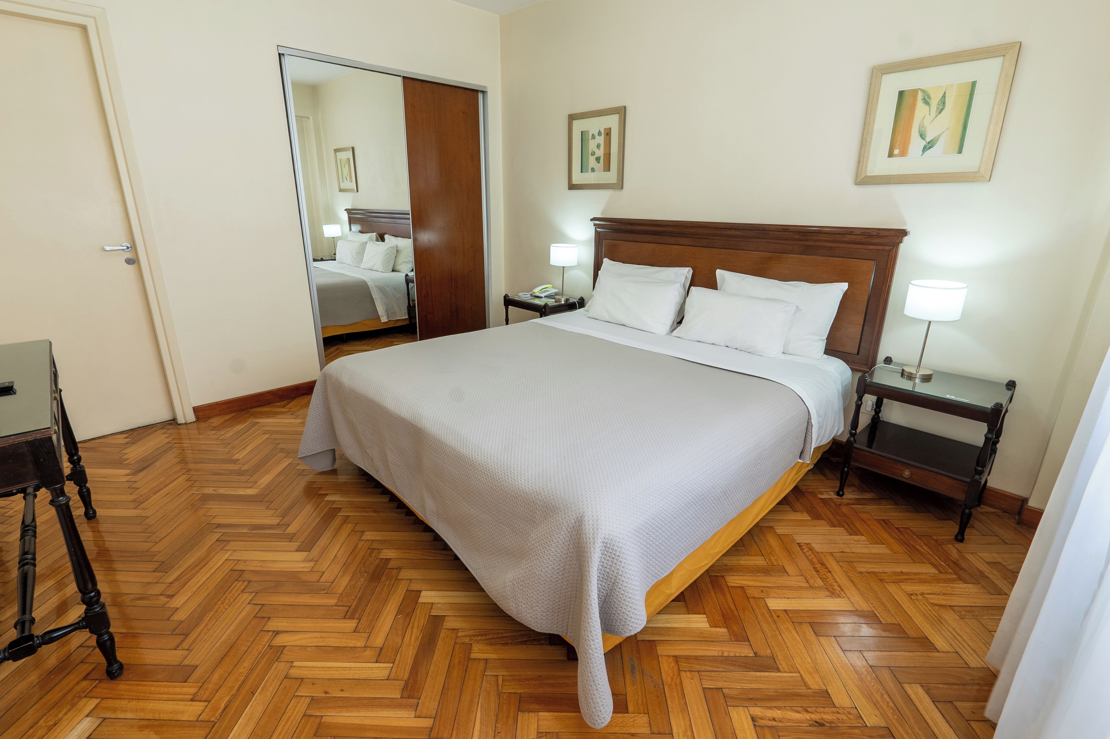 Een keurig opgemaakt hotelkamer met een groot bed, houten vloer, nachtkastjes en kunstwerken aan de wanden.