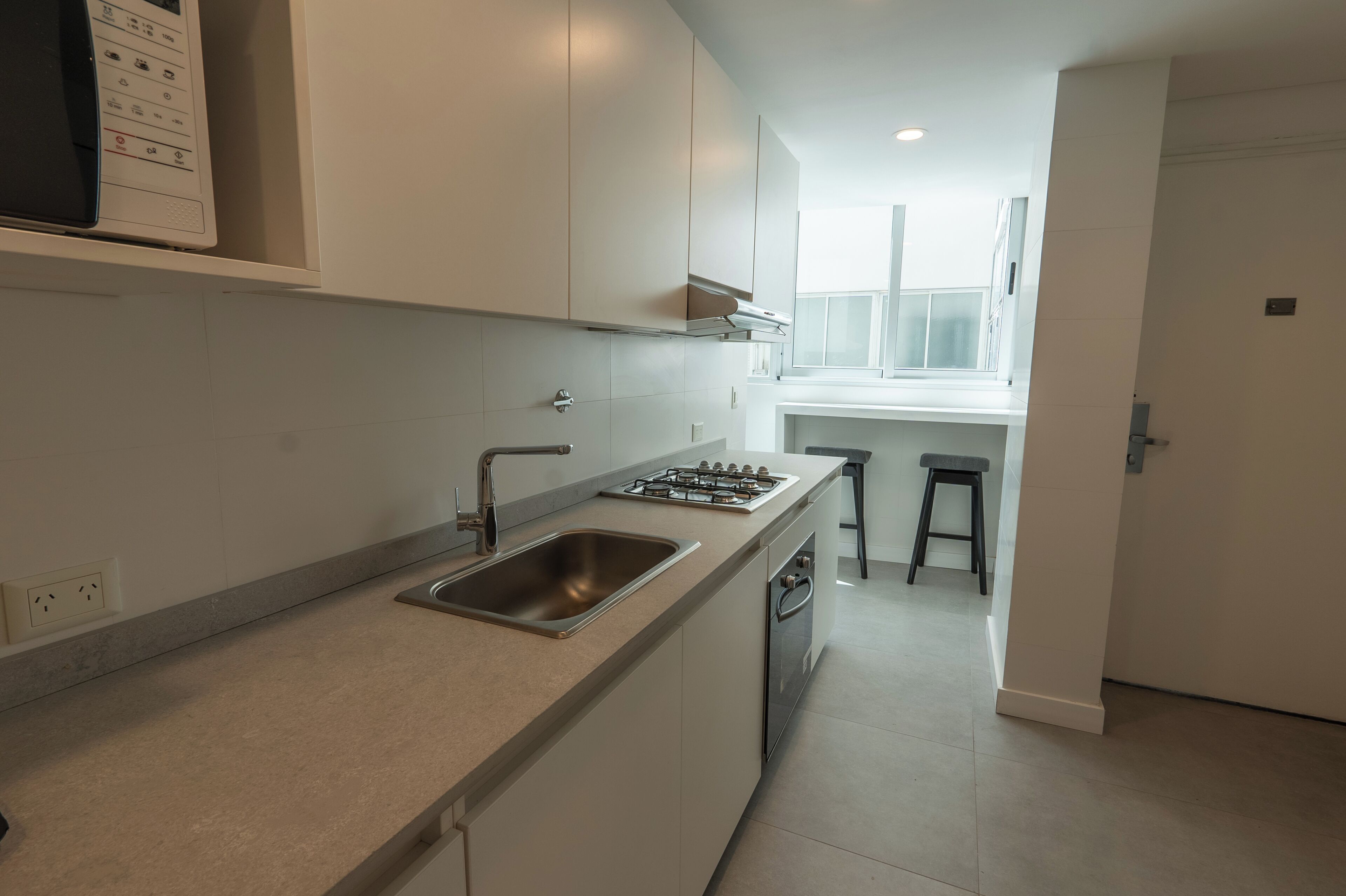 A modern kitchen with a built-in stove, sink, and bar stools.