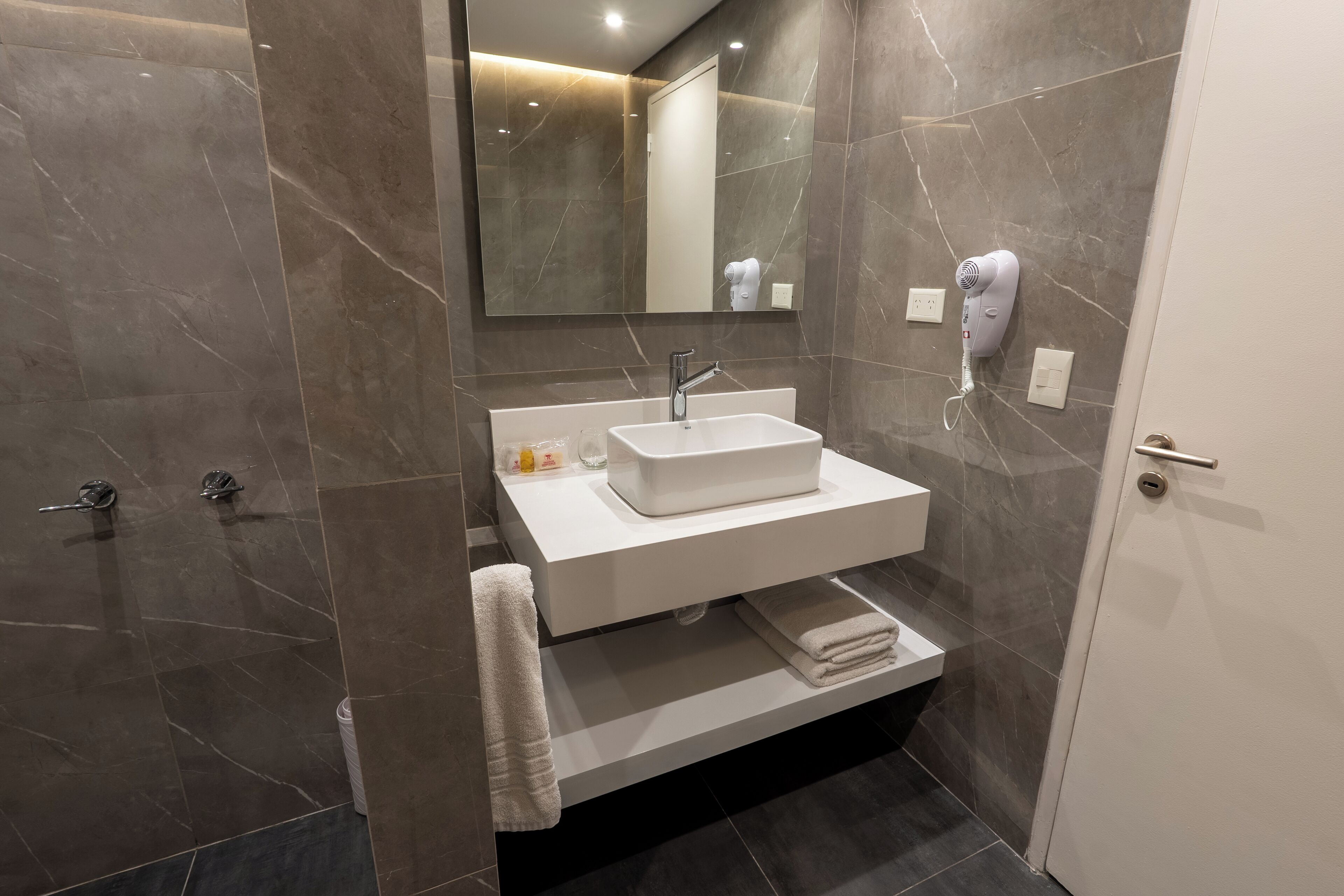 A modern bathroom with a white sink, a mirror, and a hairdryer on the wall.