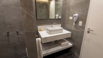 A modern bathroom with a white sink, a mirror, and a hairdryer on the wall.