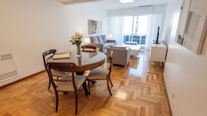 Una sala de estar moderna con comedor, que presenta un piso de madera en espiga, una mesa redonda con sillas, un sofá, una mesa de centro y un televisor.