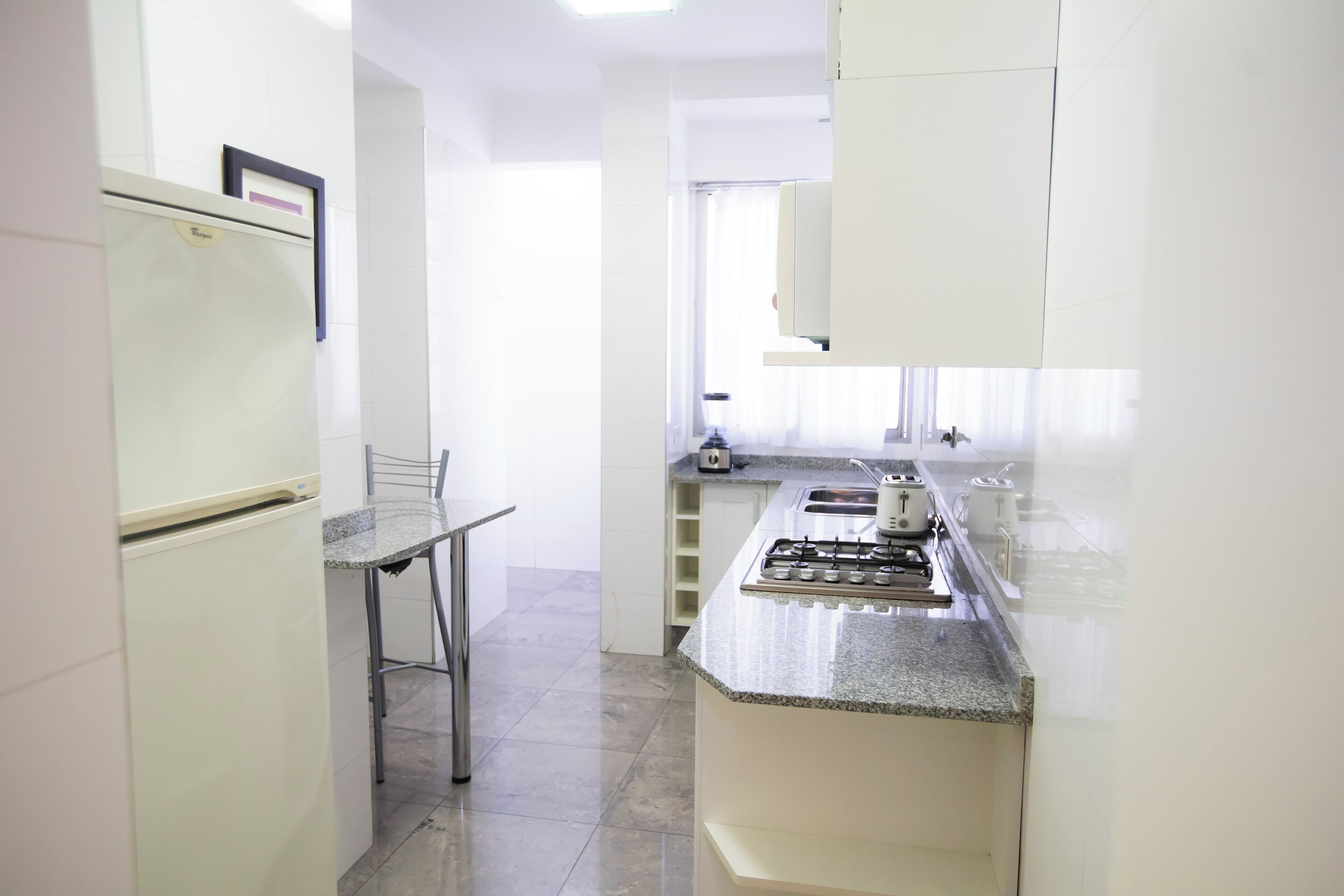 Uma cozinha compacta com geladeira, fogão a gás e um espaço de refeições com uma cadeira.