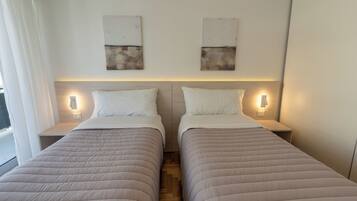 A hotel room with two beds, each with a headboard, bedside tables, and wall-mounted light fixtures.
