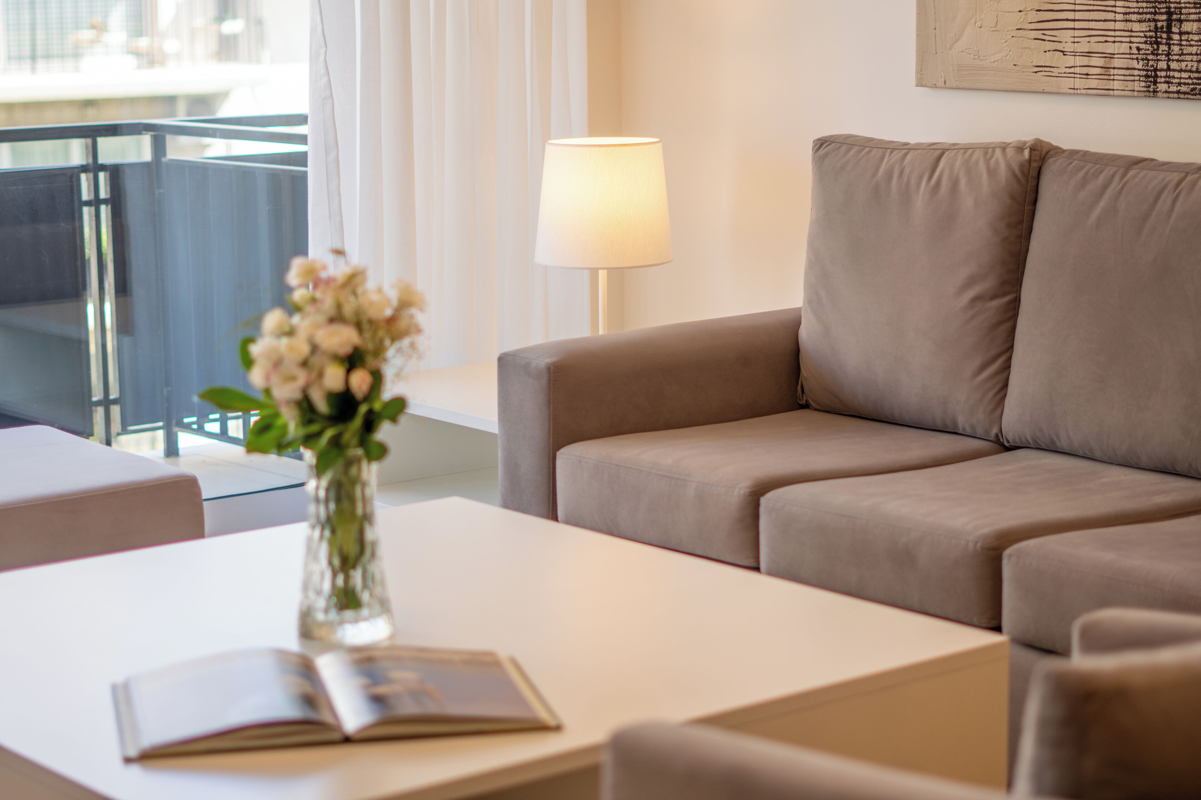 En moderne stue med en beige sofa, et hvidt sofabord og en vase med blomster.
