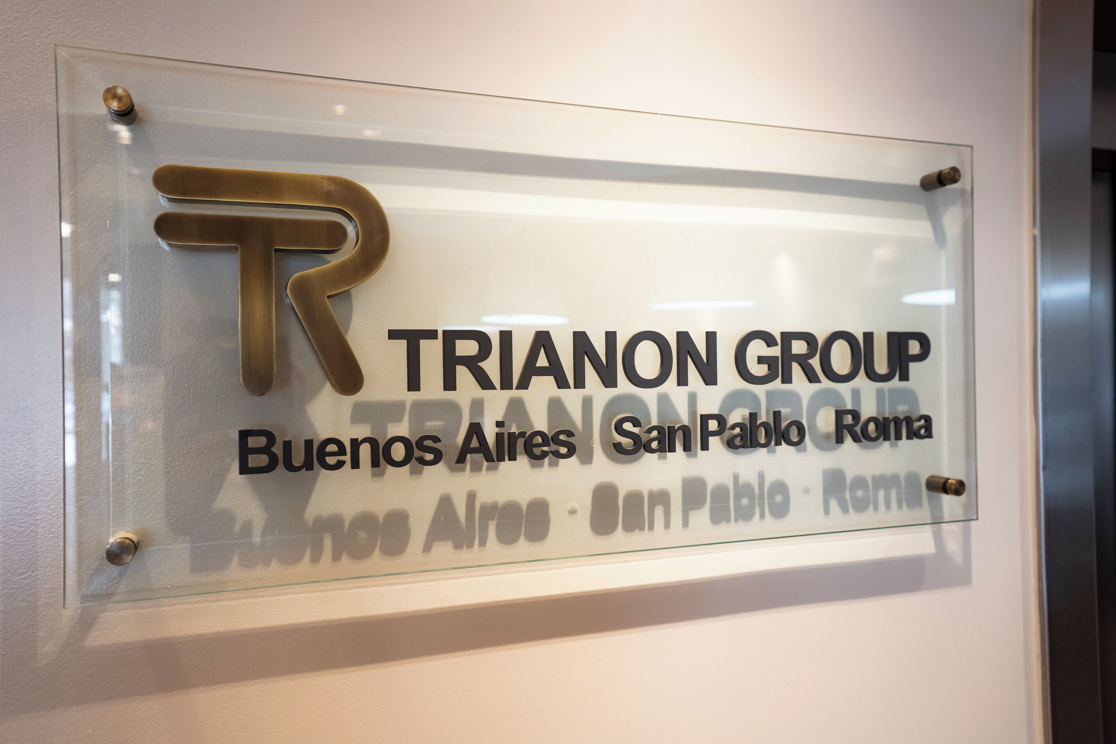 A glass sign with the text "TRIANON GROUP Buenos Aires San Pablo Roma" and a large "R" logo.