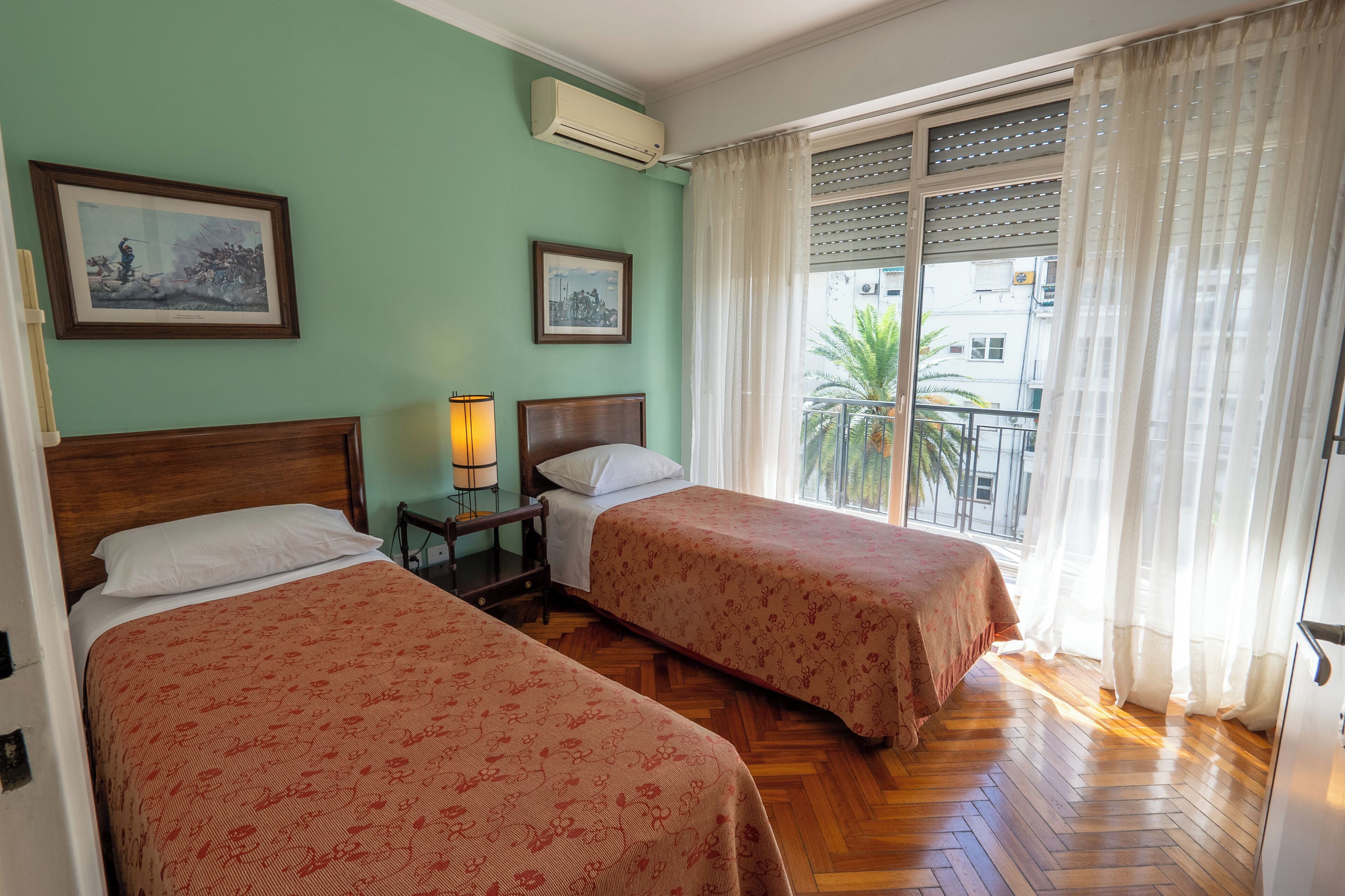 A room with two beds, a nightstand, a lamp, and a window with curtains.