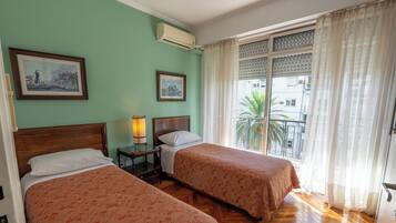 A room with two beds, a nightstand, a lamp, and a window with curtains.