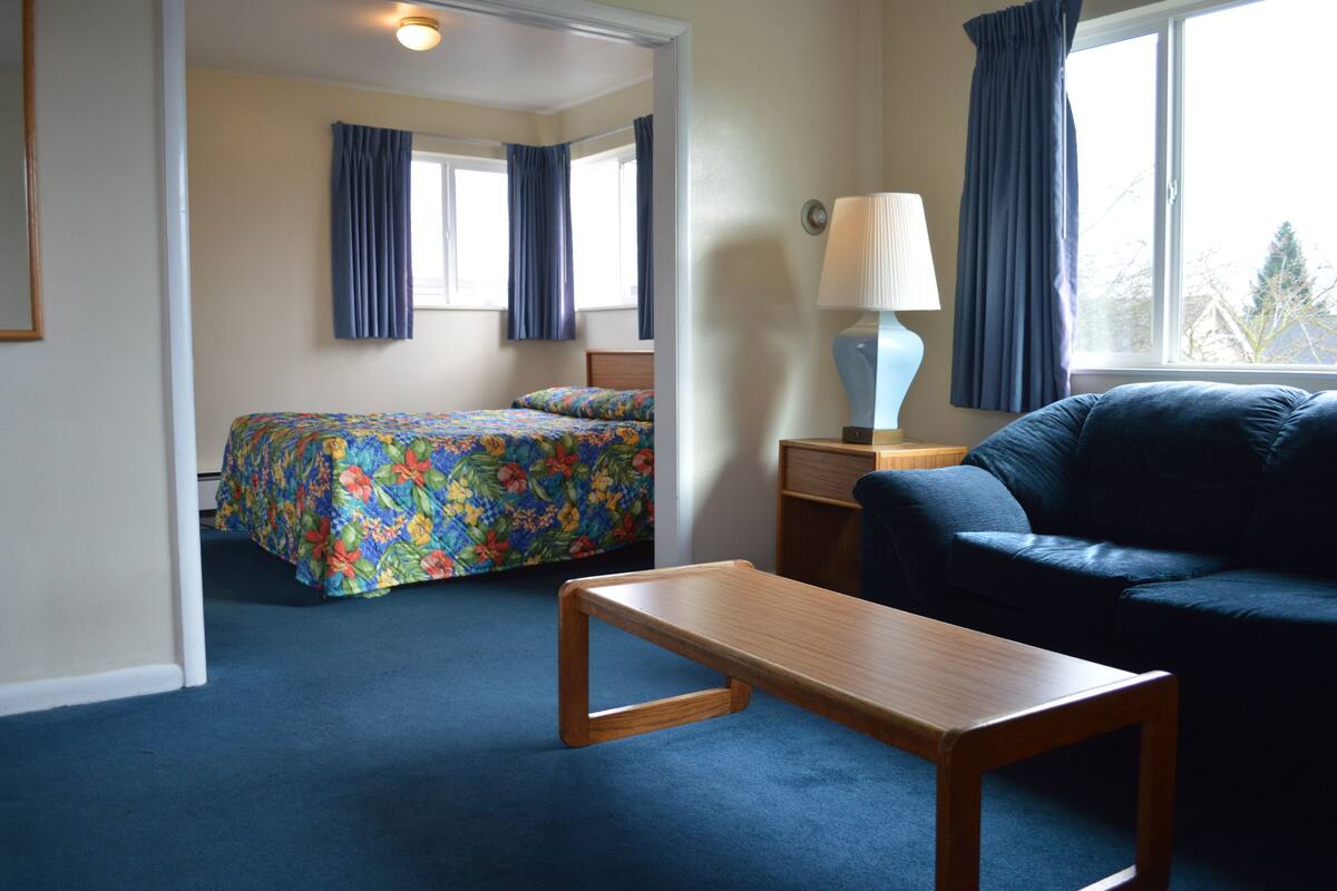 A hotel room with a bed, a sofa, a wooden table, and a lamp.