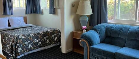 Une chambre d’hôtel avec un lit, un canapé, une table de chevet avec une lampe et une fenêtre avec des rideaux.
