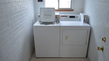 A compact, white laundry room with a washing machine and dryer, a window, and a "No Smoking" sign on the wall.