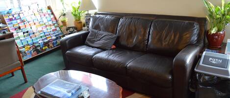 A leather sofa with a cushion, a glass coffee table with a book, a world map on the wall, and a trash bin with a 'PUSH' sign.