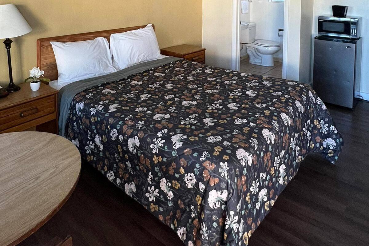 A hotel room with a bed, bedside table, lamp, and a small table.