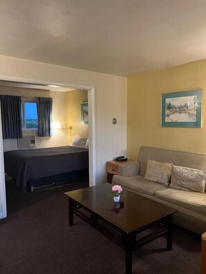 Una habitación de hotel con cama, sofá, una mesita de centro con una flor y un cuadro en la pared.