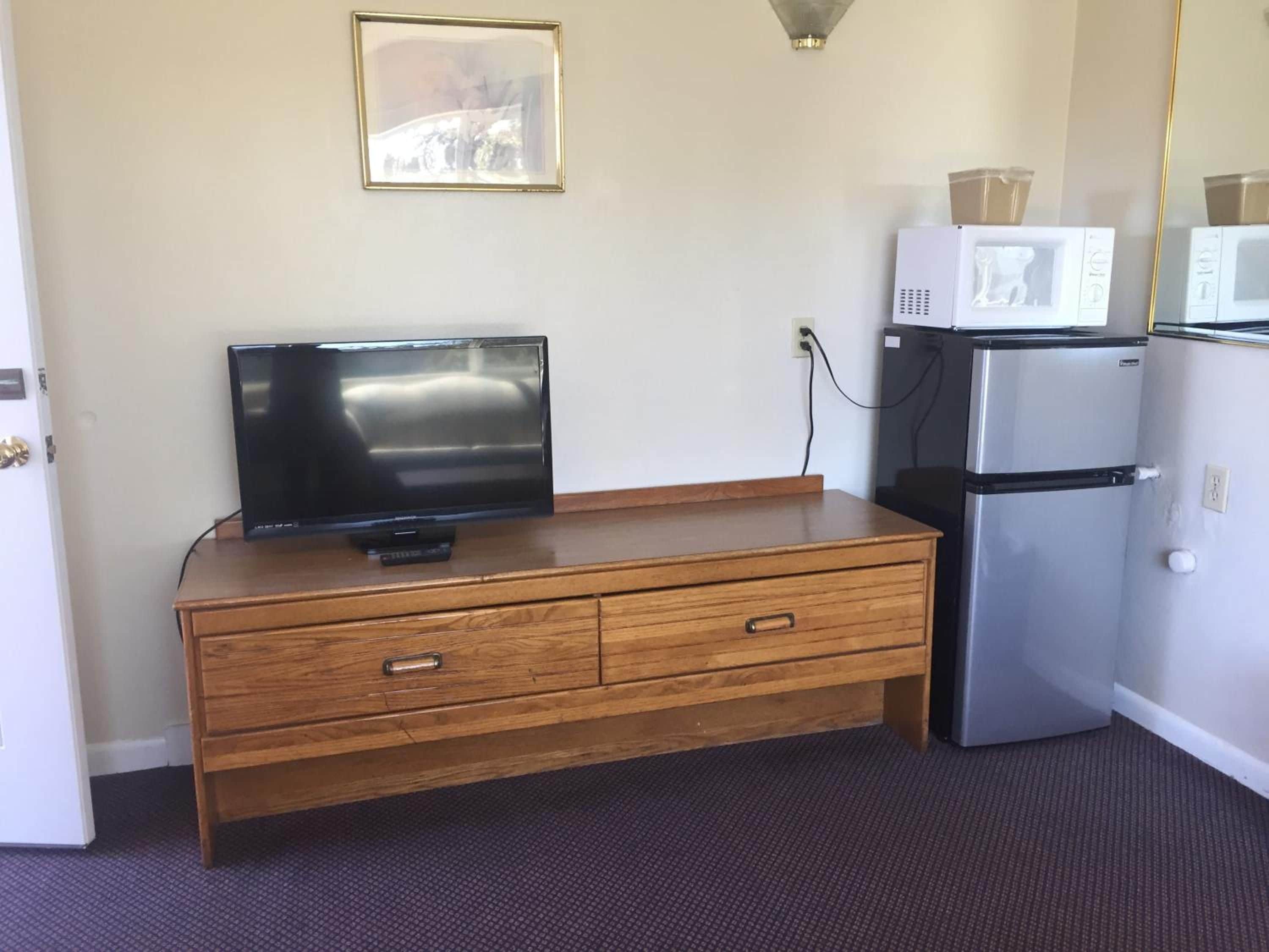 Une chambre dotée d’une commode en bois, d’un téléviseur à écran plat, d’un réfrigérateur et d’un four à micro-ondes.