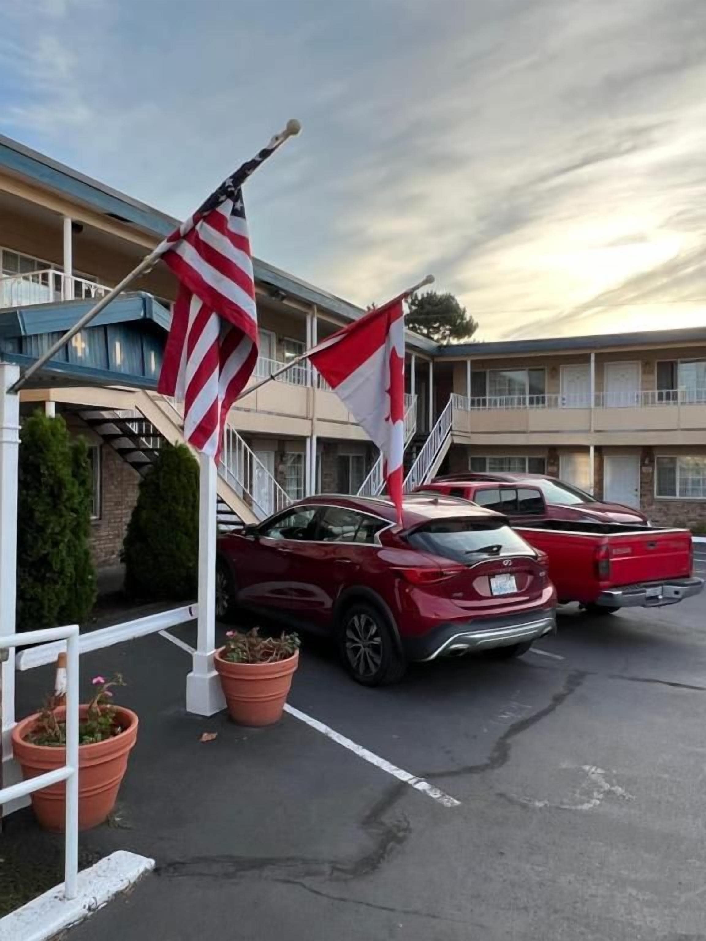 Ein Motel mit Parkplatz, zwei rote Autos und amerikanischen Flaggen.