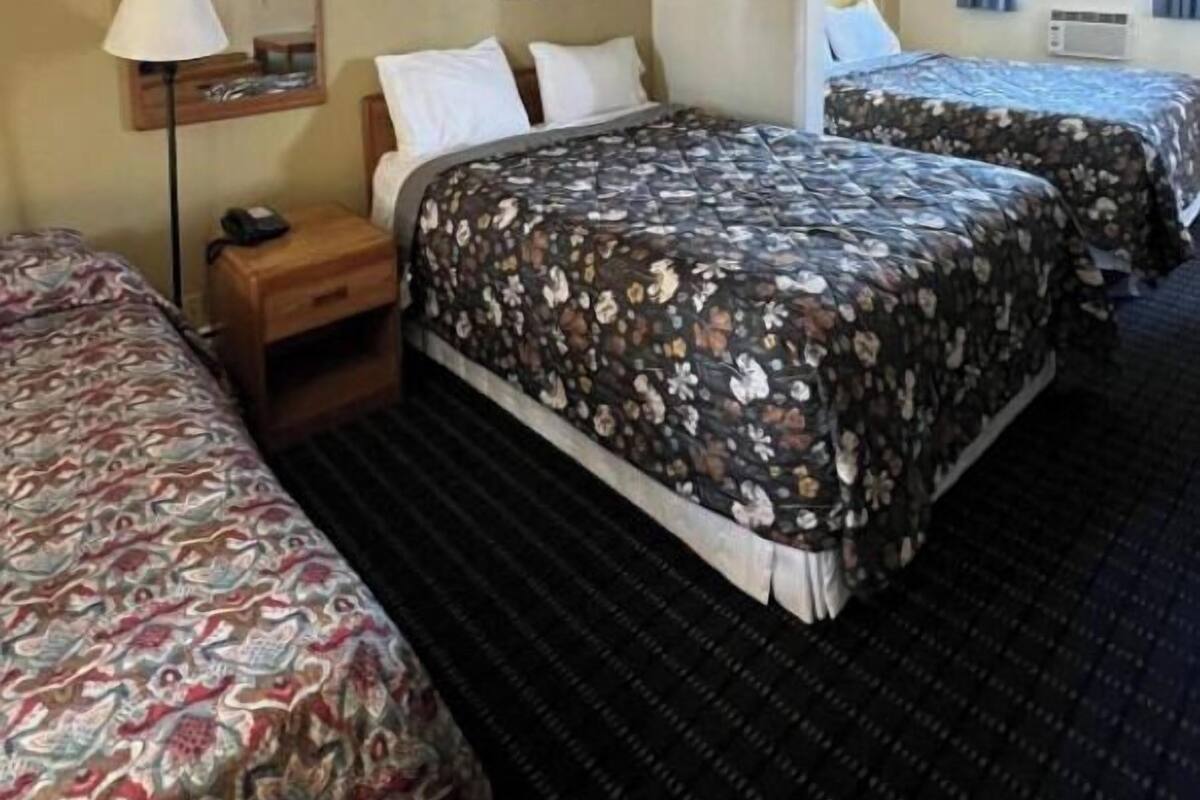 A hotel room with two beds, a nightstand, a lamp, and a mirror.