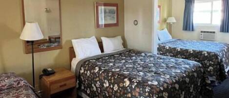 A hotel room with two beds, a nightstand, a lamp, and a mirror.