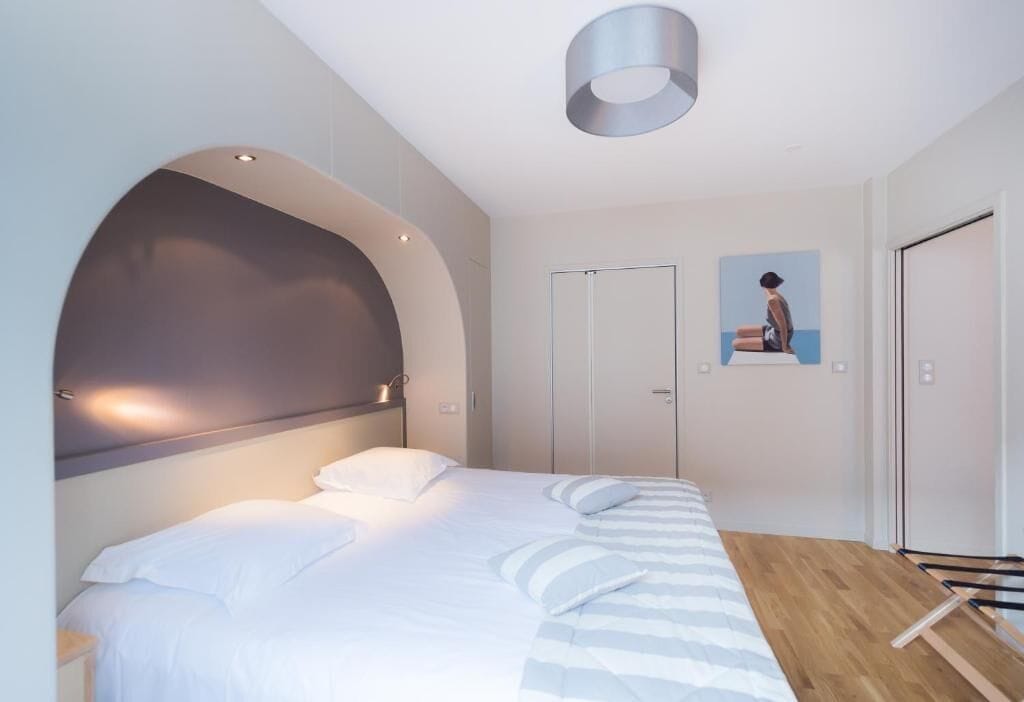A modern bedroom with a large bed, a curved headboard, a wardrobe, and a painting on the wall.