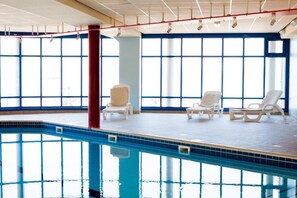 An indoor swimming pool with clear blue water, white lounge chairs, and large windows allowing natural light. - Les Résidences d'Armor (Douarnenez)