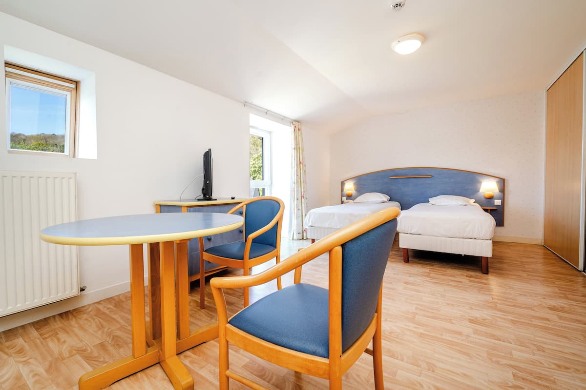 A room with a bed, two chairs, a small table, a radiator, and a window with a view.