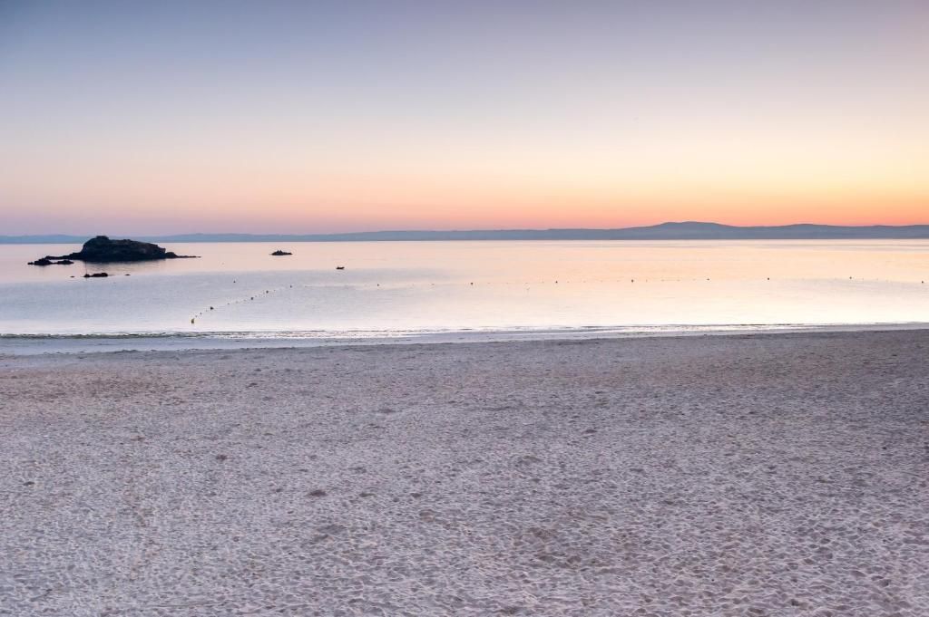 A beach with a calm sea, a distant landmass, and a clear sky.