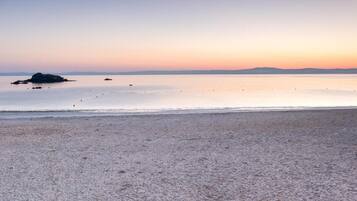 A beach with a calm sea, a distant landmass, and a clear sky.