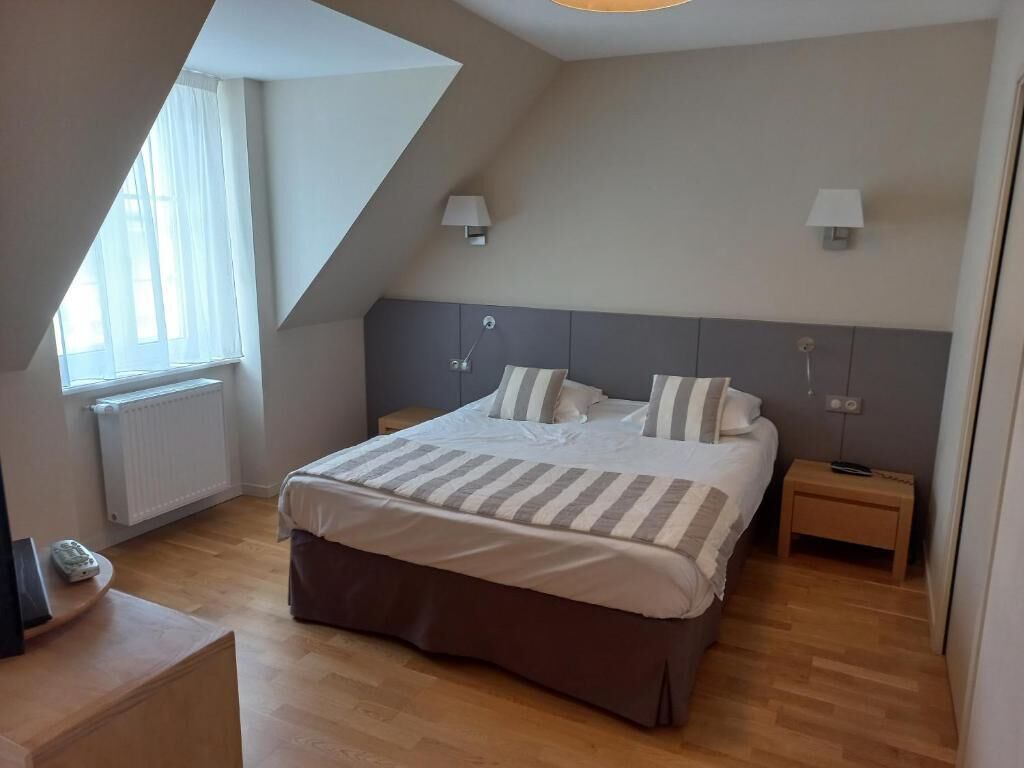 A bedroom with a large bed, two bedside tables, a window with curtains, and a radiator.