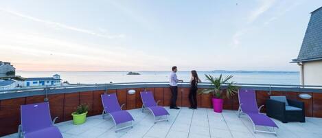 Terraza en la azotea con sillones de descanso, plantas en macetas y vista al mar.