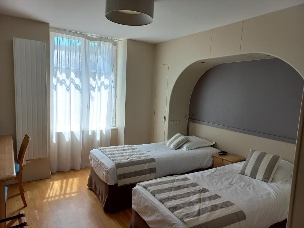 Hotellihuone, jossa on kaksi sänkyä, työpöytä ja tuoli.