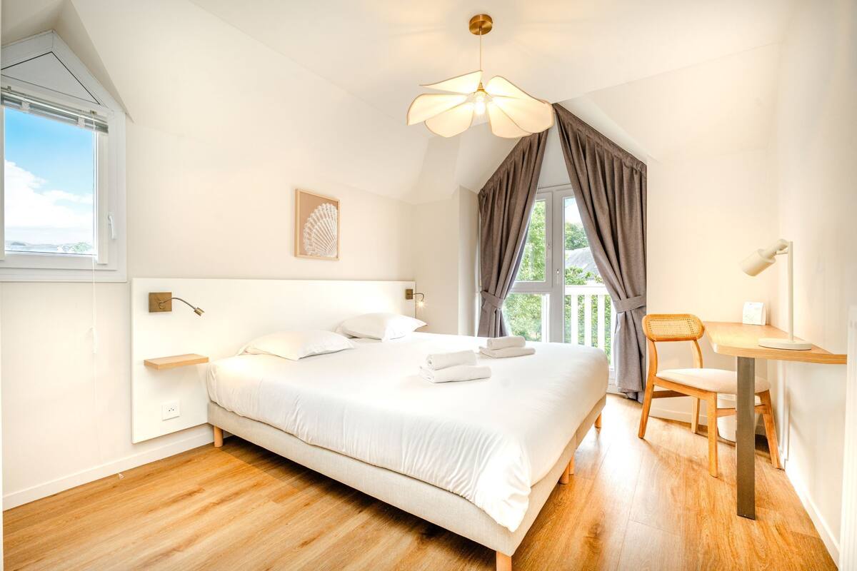 A bedroom with a bed, bedside table, chair, and a view of the outdoors.