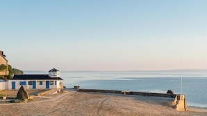 A coastal building with a lighthouse, a sandy beach, and a calm sea.