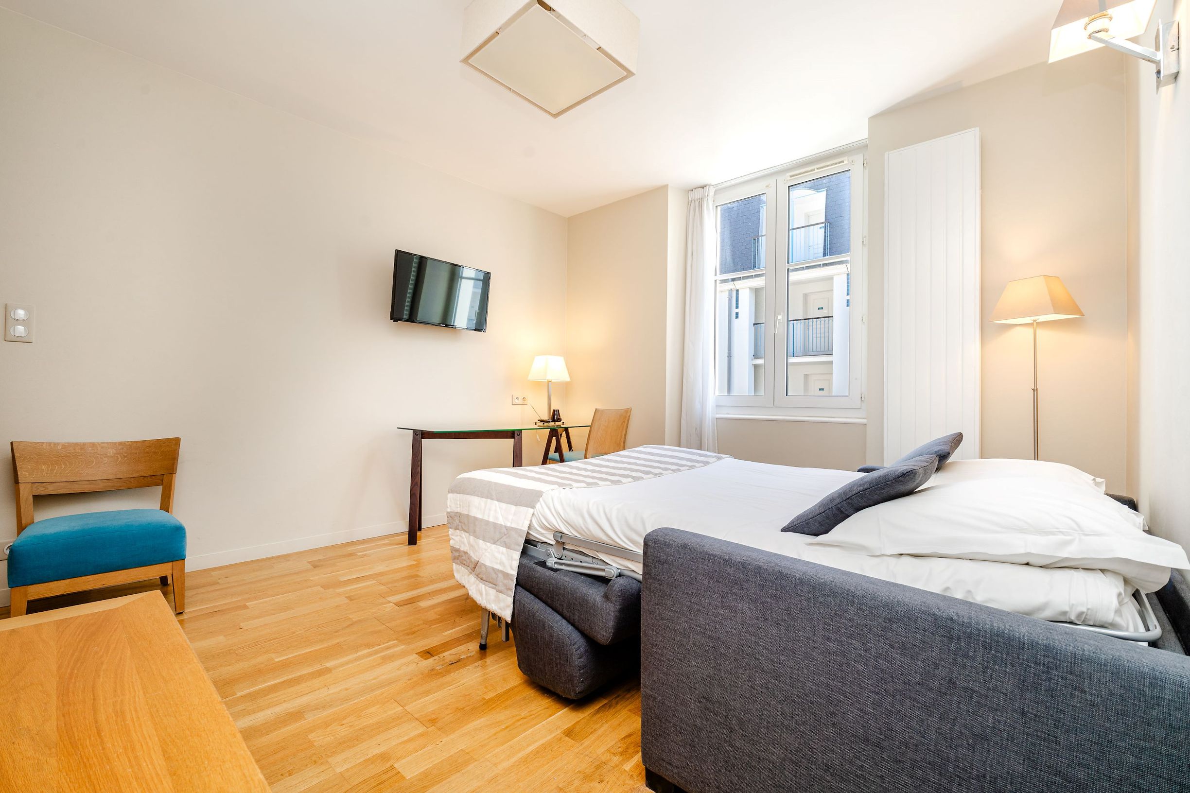 A hotel room with a bed, a desk, a chair, a TV, and a window.