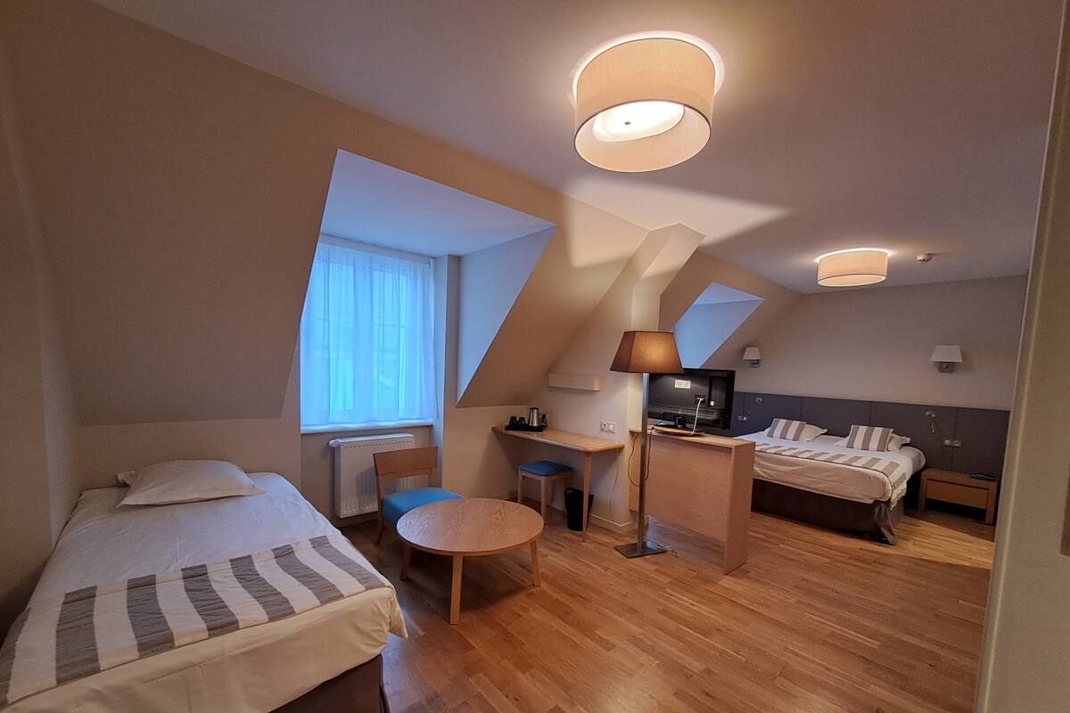 A modern hotel room with two beds, a desk, and a small seating area.