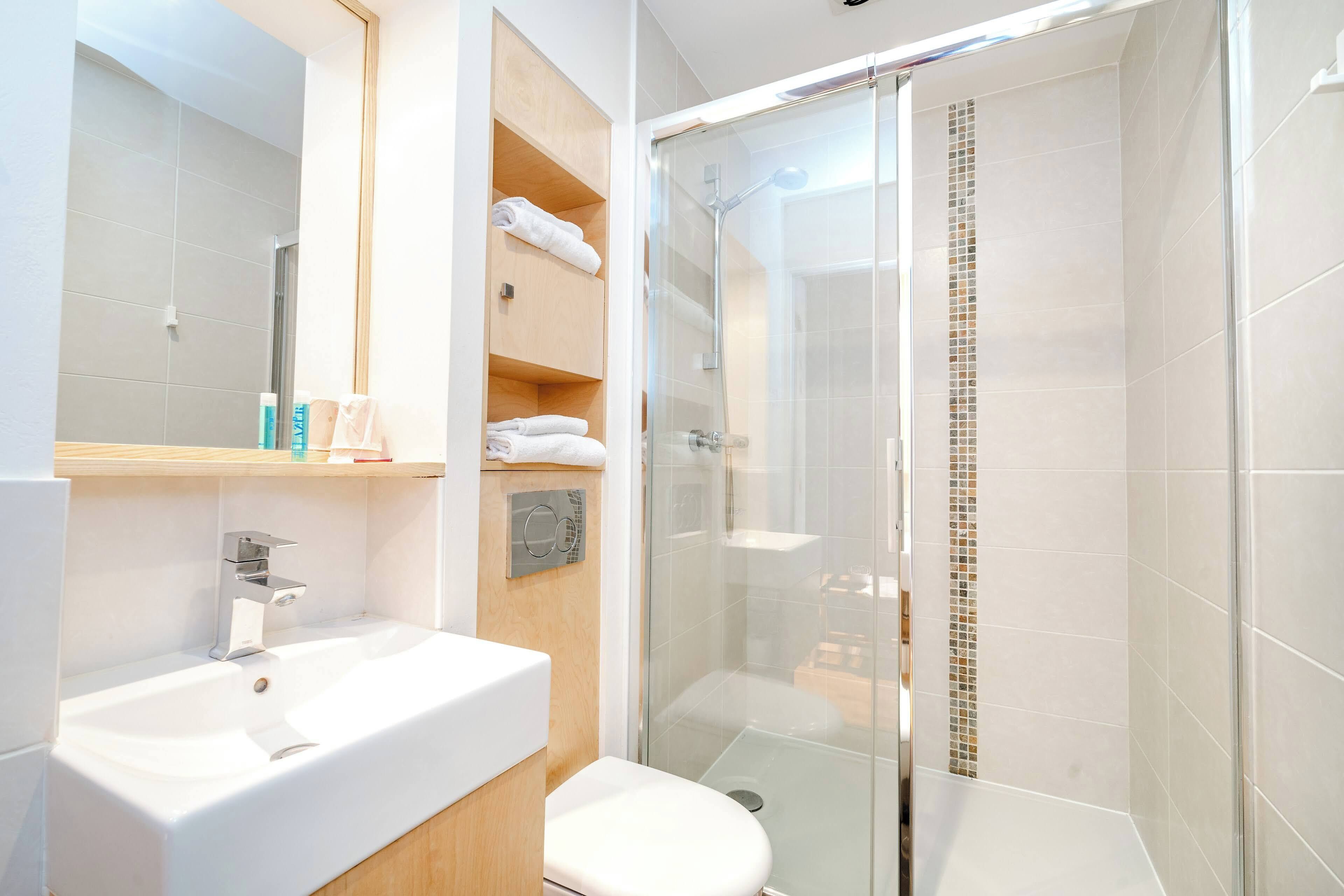 Un baño moderno con ducha acristalada, lavamanos blanco y un inodoro.