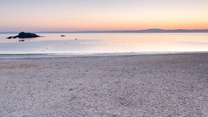 A beach with a calm sea, a distant landmass, and a clear sky.