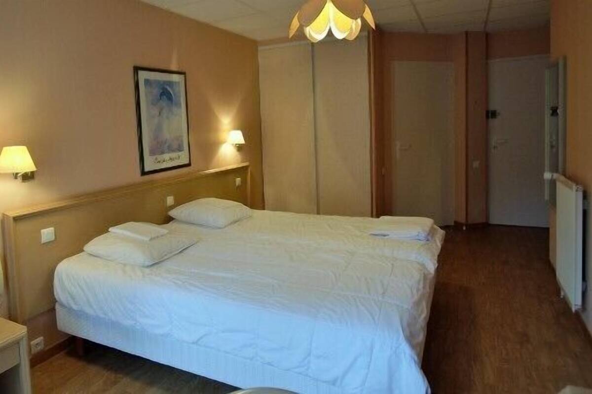 A hotel room with a large bed, two bedside lamps, a framed picture on the wall, and a wardrobe.