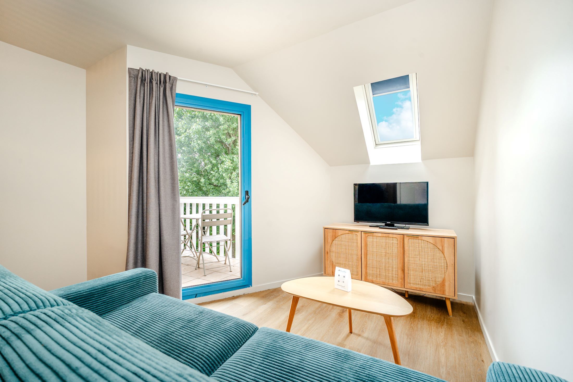 Ein Wohnzimmer mit einer Couch, einem Fernseher auf einer Holzkommode, einem kleinen Tisch und einer Glasschiebetür, die zu einem Außenbereich führt.